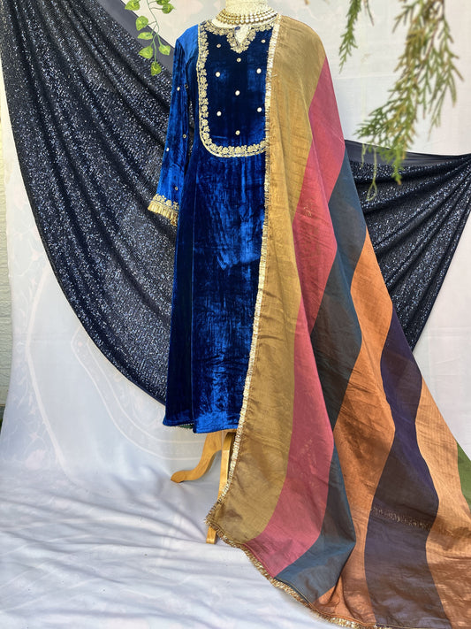 A folded royal blue velvet garment with gold embroidery and a striped multicolor dupatta draped over a black sequined fabric on a white background.